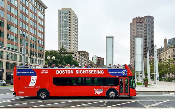 Red double-decker bus on Boston Hop-On Hop-Off tour with city buildings in the background.