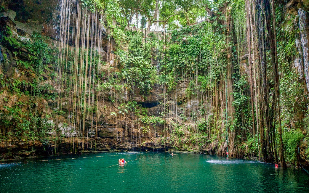 Swimmers in Cenote Chichen Itza surrounded by lush vegetation, Yucatan, Mexico.