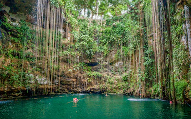 Swimmers in Cenote Chichen Itza surrounded by lush vegetation, Yucatan, Mexico.