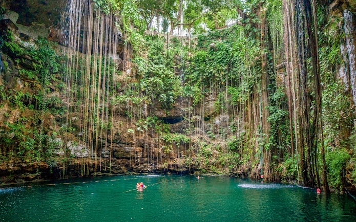 Swimmers in Cenote Chichen Itza surrounded by lush vegetation, Yucatan, Mexico.