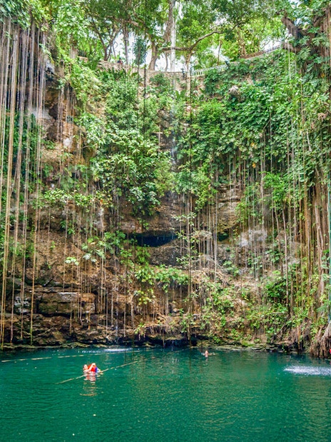 Swimmers in Cenote Chichen Itza surrounded by lush vegetation, Yucatan, Mexico.