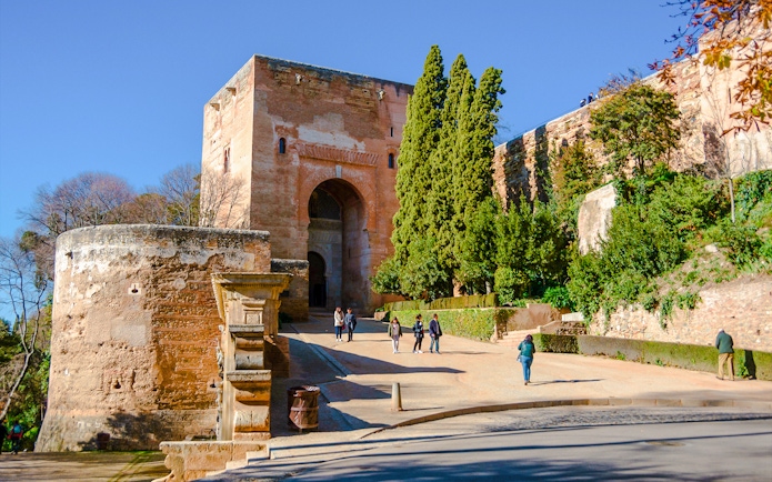 Gate of Justice at Alhambra, Granada, with visitors walking towards the entrance.