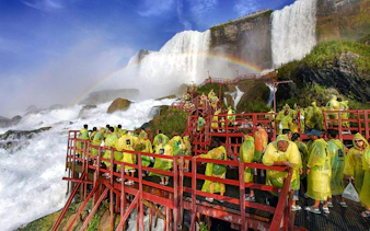 Visitors in yellow ponchos on red walkways at Cave of the Winds, Niagara Falls, with a rainbow overhead.