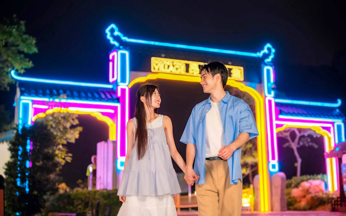 Couple holding hands in front of neon lights at Ngong Ping 360, Lantau Island.