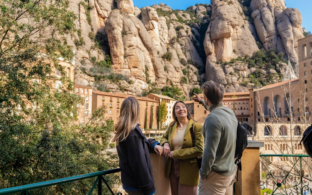 Tourists with guide at Montserrat mountain viewpoint, Spain, admiring rocky landscape.