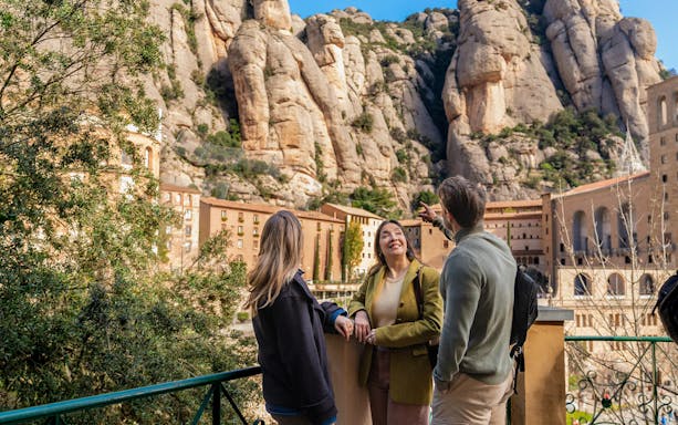 Tourists with guide at Montserrat mountain viewpoint, Spain, admiring rocky landscape.
