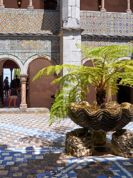 Cloisters with ornate arches and a central fern in a shell-shaped planter.