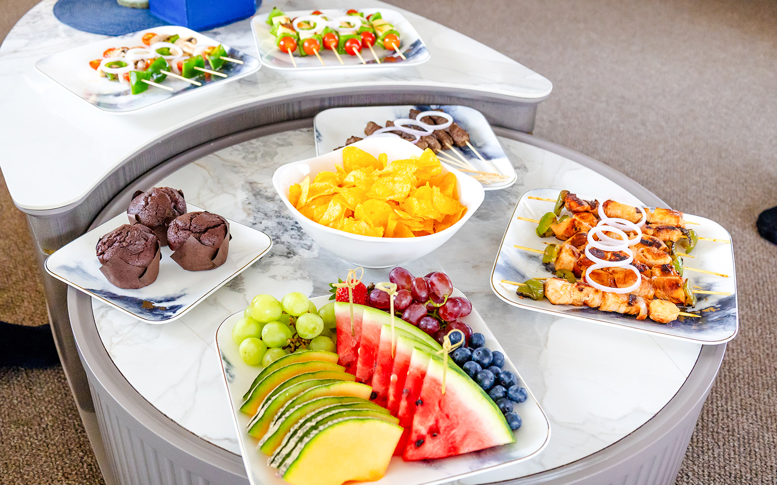 Fruits and snacks on a yacht table with skewers, chips, and muffins.