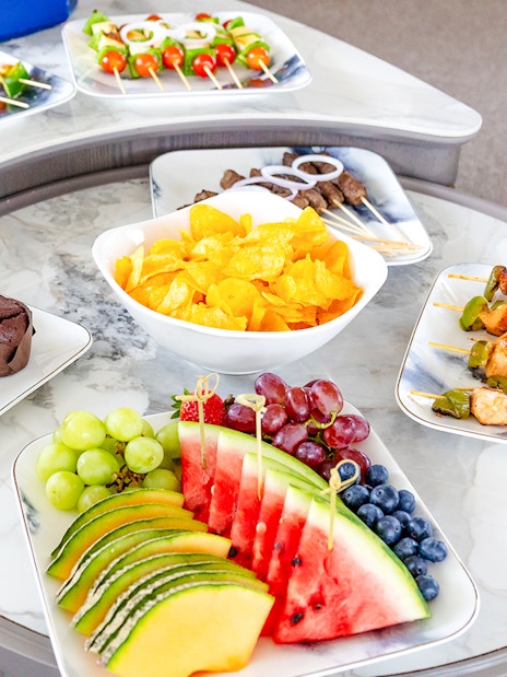Fruits and snacks on a yacht table with skewers, chips, and muffins.