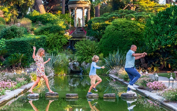 Family crossing stepping stones in a lush garden on the French Riviera.
