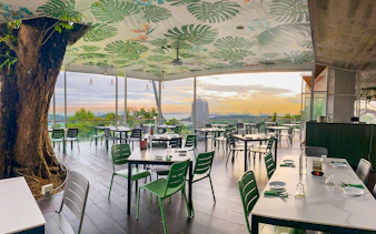 Outdoor dining area with view of Singapore skyline at sunset, featuring lush greenery and modern decor.