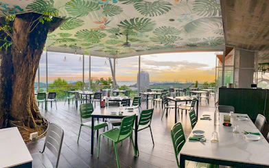 Outdoor dining area with view of Singapore skyline at sunset, featuring lush greenery and modern decor.