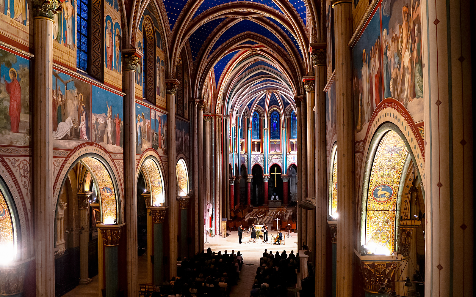 Orchestra performing inside St Germain des Prés Church, Paris, with illuminated arches and frescoes.