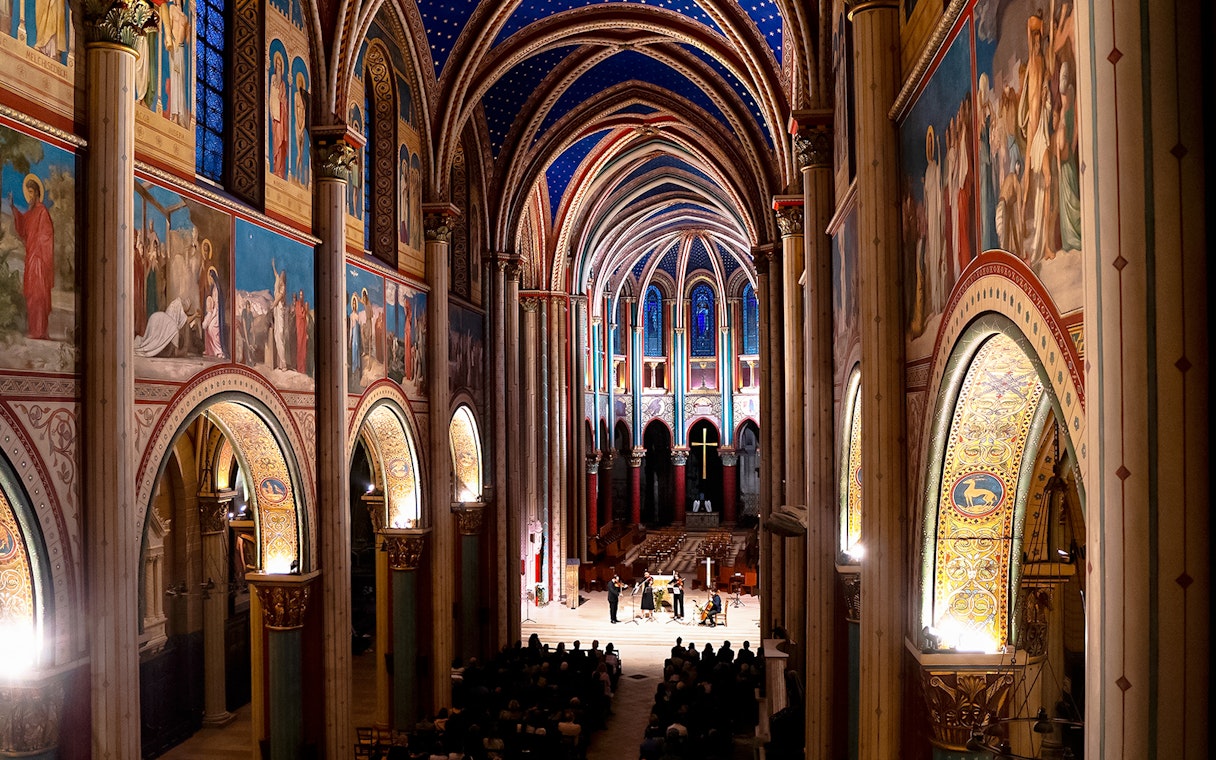 Orchestra performing inside St Germain des Prés Church, Paris, with illuminated arches and frescoes.