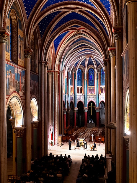 Orchestra performing inside St Germain des Prés Church, Paris, with illuminated arches and frescoes.
