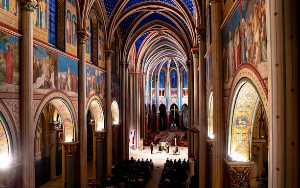 Orchestra performing inside St Germain des Prés Church, Paris, with illuminated arches and frescoes.