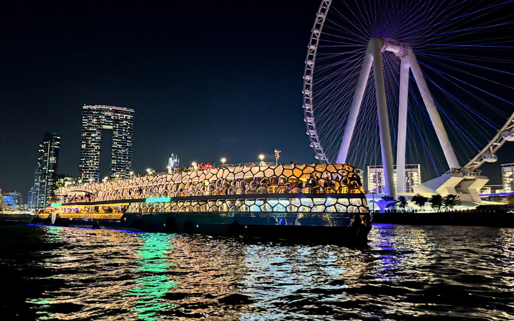 Cruise ship illuminated at night near a large Ferris wheel on the sea.