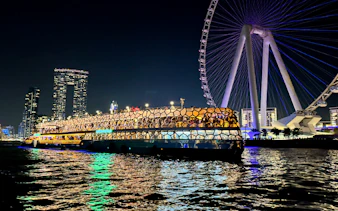 Cruise ship illuminated at night near a large Ferris wheel on the sea.