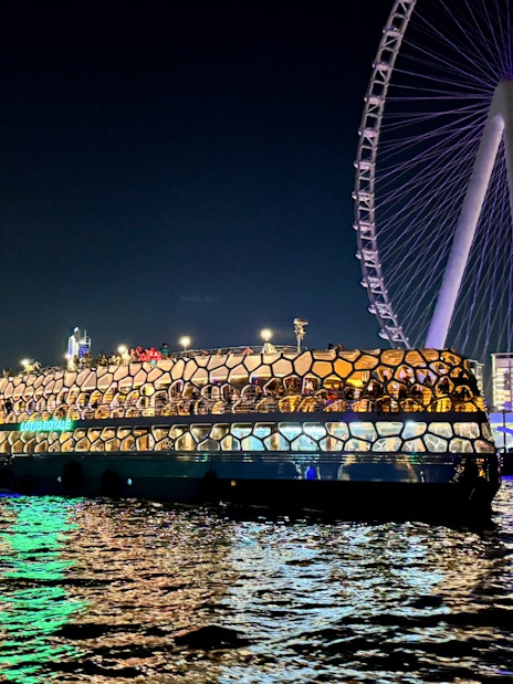 Cruise ship illuminated at night near a large Ferris wheel on the sea.