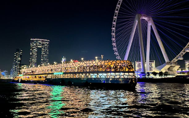 Cruise ship illuminated at night near a large Ferris wheel on the sea.
