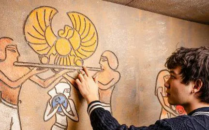 Young man interacting with Egyptian-themed wall puzzle in Curse of the Pharaoh Escape Room, Dubai.