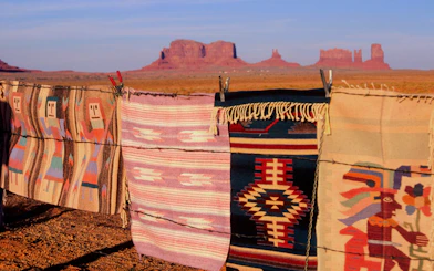 Traditional Navajo rugs on barbed wire with Monument Valley buttes in the background.