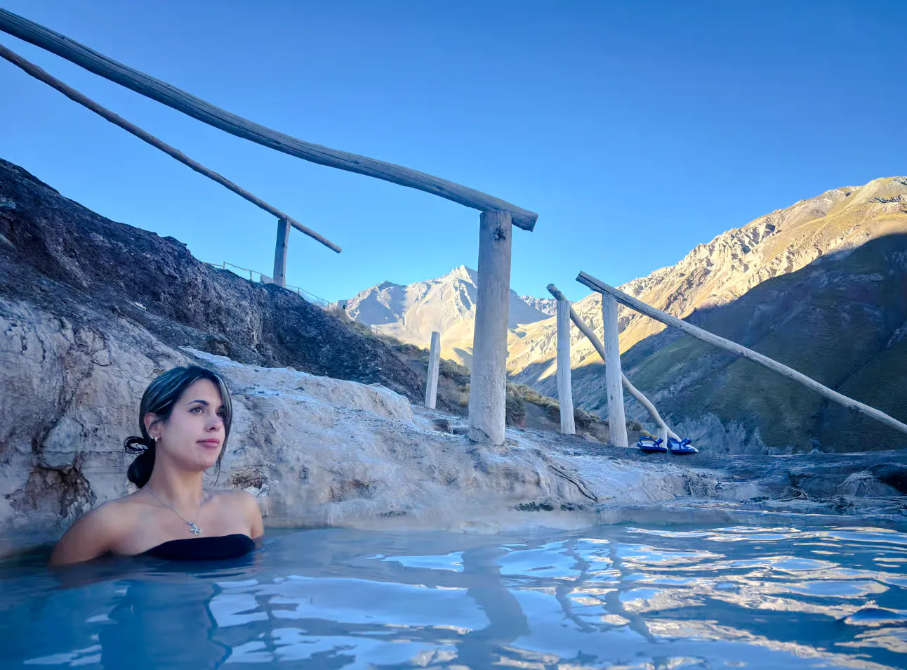 Person relaxing in thermal pool at Termas Baños Colina, with Andes mountains in Cajon del Maipo, Santiago.