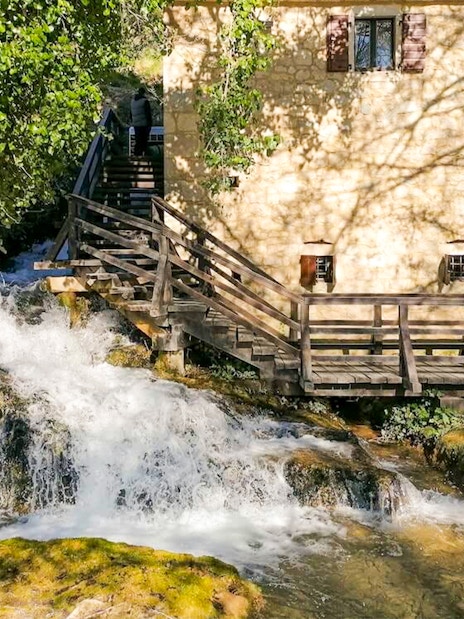 Stone building and wooden bridge over a waterfall in Krka National Park, Croatia.