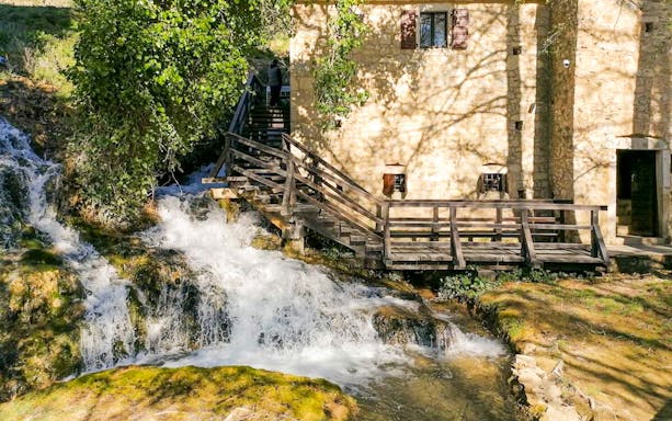 Stone building and wooden bridge over a waterfall in Krka National Park, Croatia.