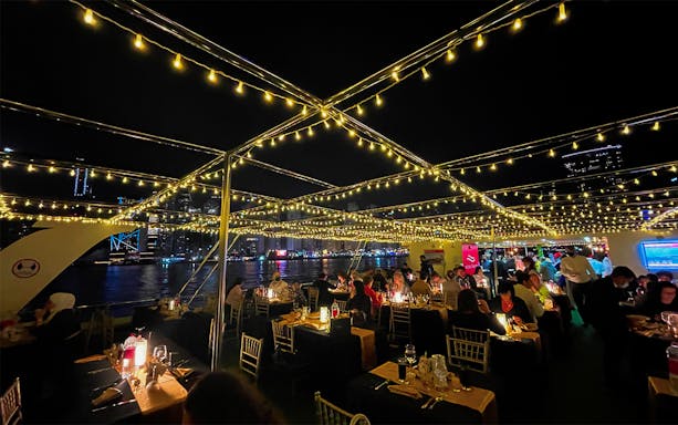 Guests dining under string lights on a marina dinner cruise with live music.