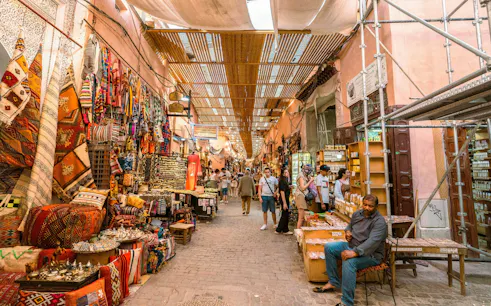 Bazaar in Marrakech, Morocco with colorful textiles and bustling shoppers.