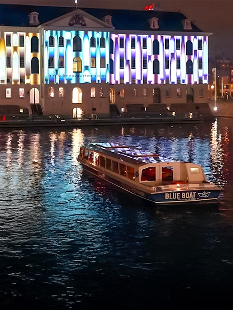 Evening cruise boat on Amsterdam canal with illuminated building during Light Festival.