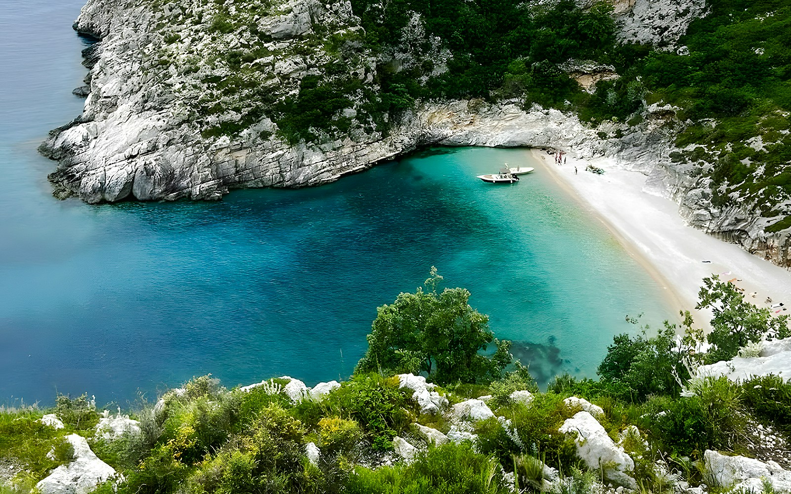 Grama Bay, Albania with turquoise waters, rocky cliffs, and a boat near the sandy shore.