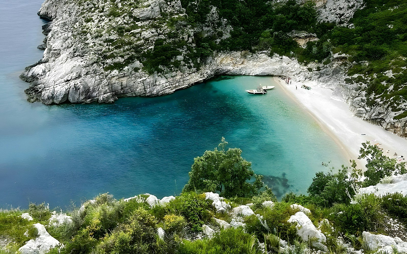 Grama Bay, Albania with turquoise waters, rocky cliffs, and a boat near the sandy shore.