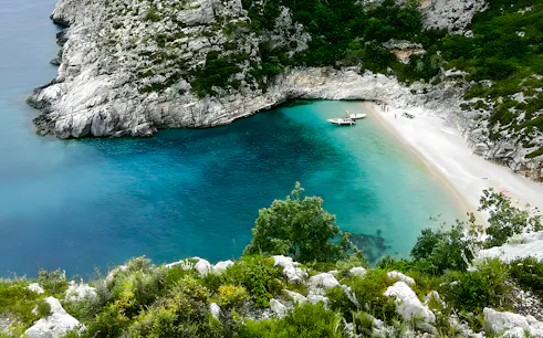 Grama Bay, Albania with turquoise waters, rocky cliffs, and a boat near the sandy shore.