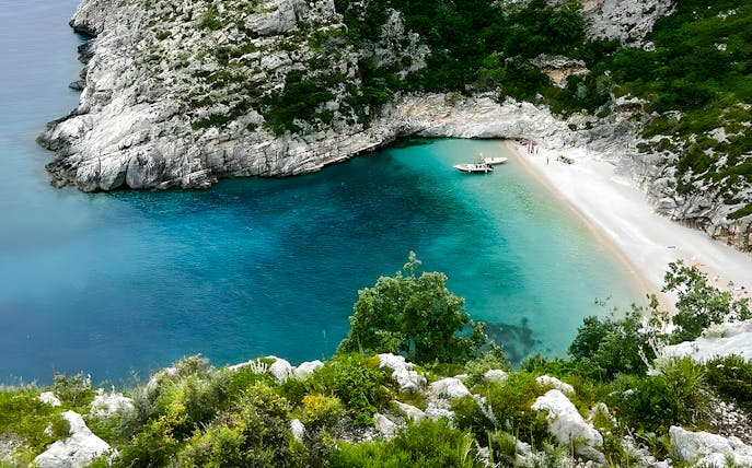 Grama Bay, Albania with turquoise waters, rocky cliffs, and a boat near the sandy shore.