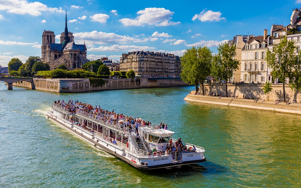 Seine River cruise boat with tourists near Notre-Dame Cathedral, Paris.