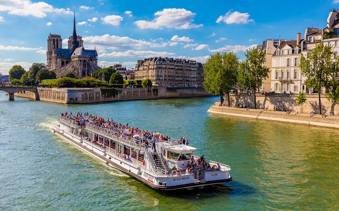Seine River cruise boat with tourists near Notre-Dame Cathedral, Paris.