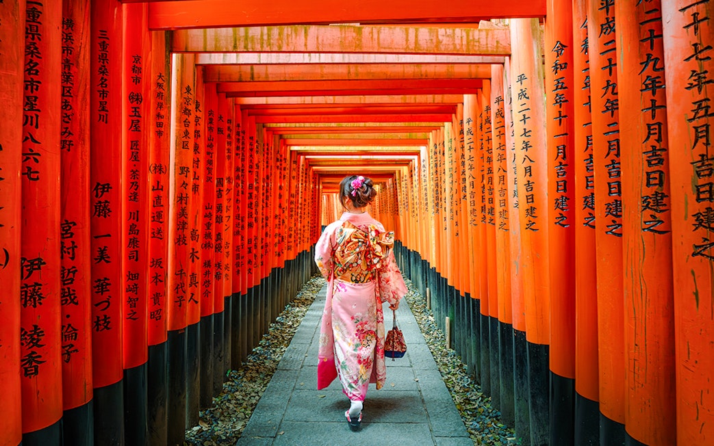 Woman in kimono walking through Fushimi Inari Shrine torii gates, Kyoto.