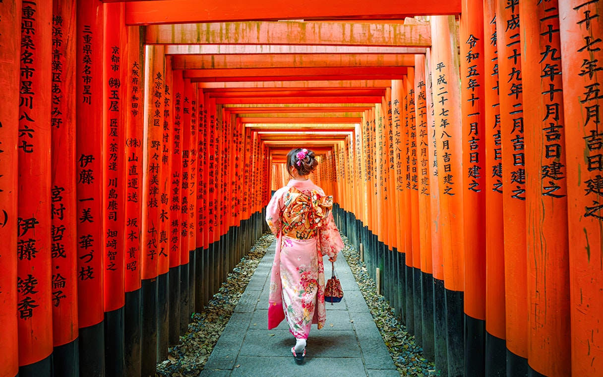 Woman in kimono walking through Fushimi Inari Shrine torii gates, Kyoto.