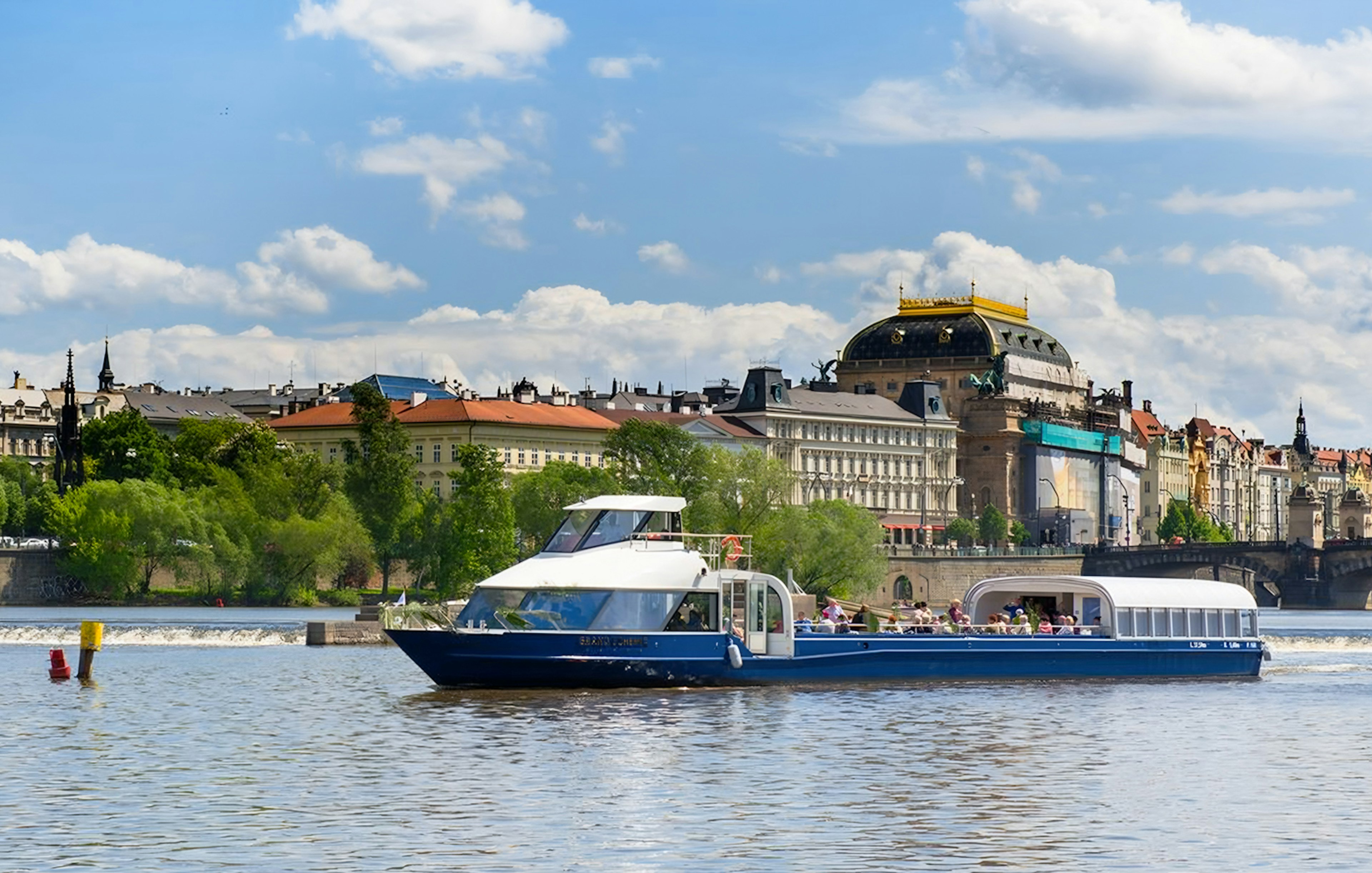 Sightseeing cruise on Vltava River with historic Prague buildings in the background.