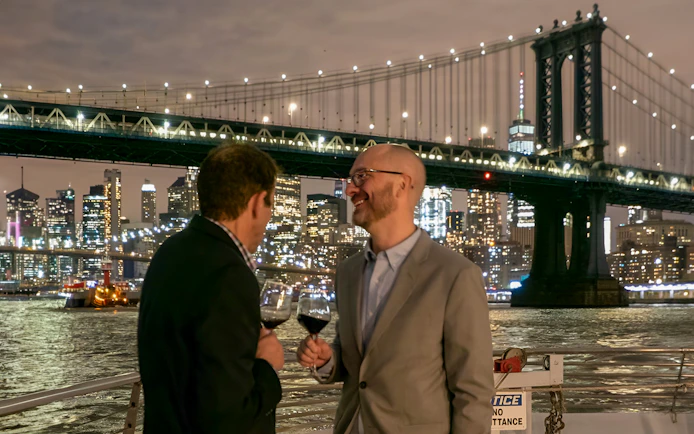 Two guests enjoying drinks with the NYC skyline and bridge in the background.