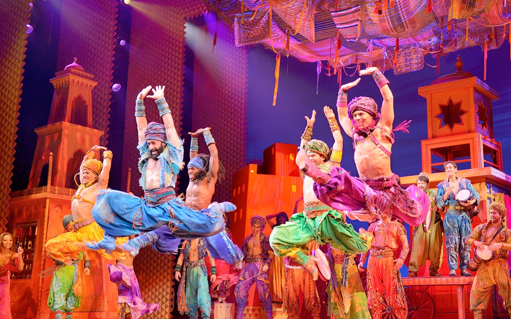 Performers in colorful costumes dancing on stage in an Aladdin musical production.