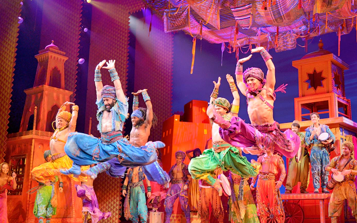 Performers in colorful costumes dancing on stage in an Aladdin musical production.