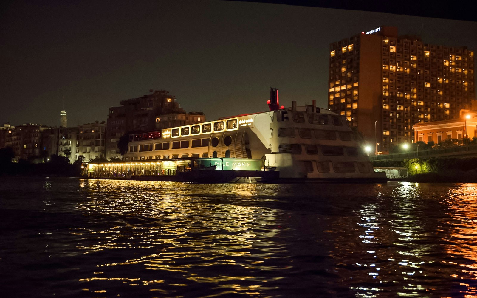 Luxury dinner cruise ship on the Nile River at night, Cairo skyline in background.