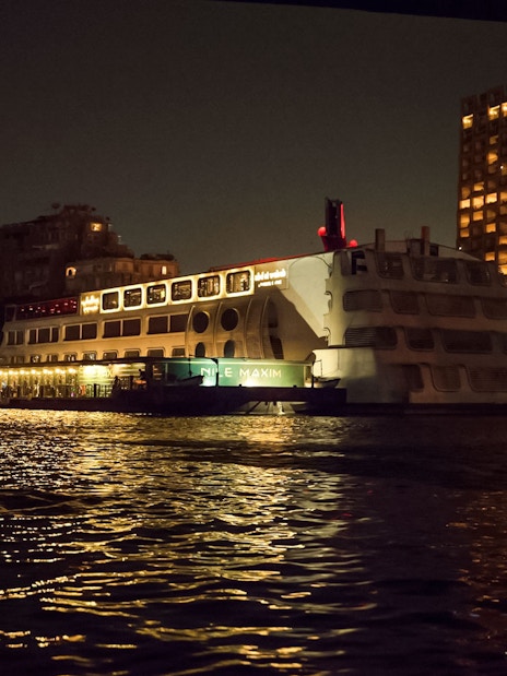 Luxury dinner cruise ship on the Nile River at night, Cairo skyline in background.