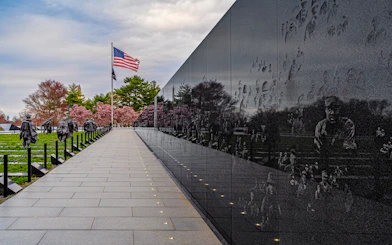 Korean War Memorial statues and wall reflections in Washington D.C. with American flag.