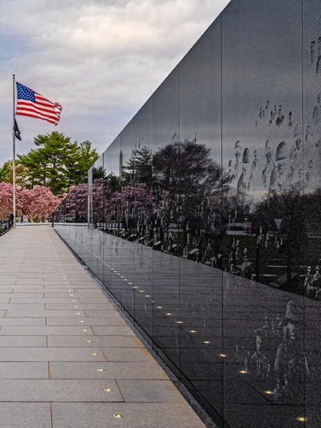 Korean War Memorial statues and wall reflections in Washington D.C. with American flag.