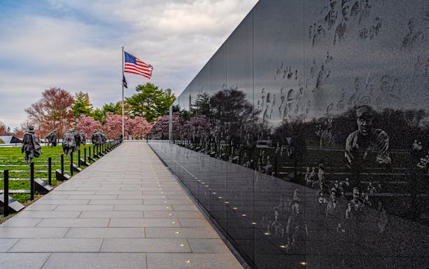 Korean War Memorial statues and wall reflections in Washington D.C. with American flag.