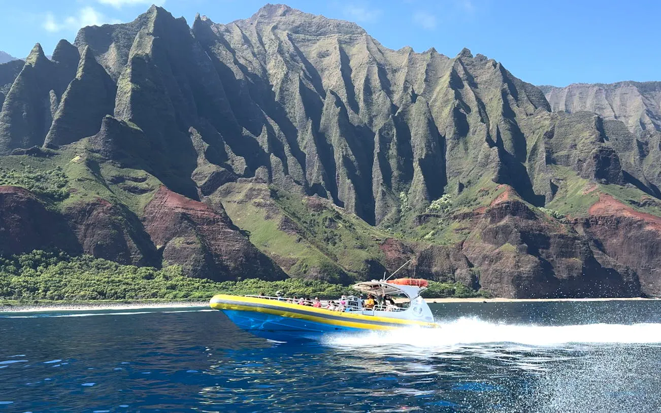Raft speeding along NaPali Coast cliffs during afternoon snorkel tour in Hawaii.